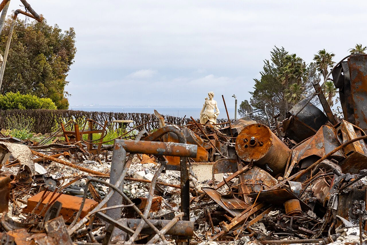 Wildfire-damaged Malibu home reduced to rusted debris with an intact garden statue overlooking the Pacific Ocean, awaiting Army Corps of Engineers debris removal after the January 2025 Palisades Fire