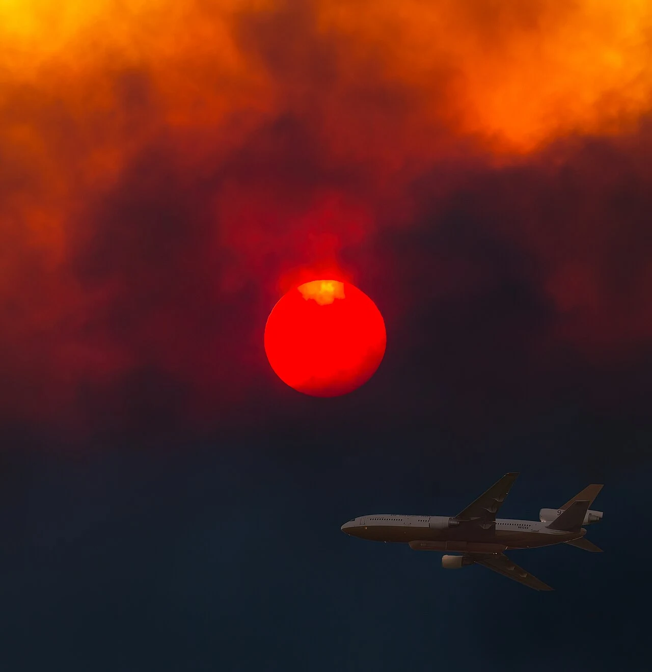 A DC-10 air tanker silhouetted below a deep red sun obscured by thick smoke during the 2018 Woolsey Fire in the Santa Monica Mountains