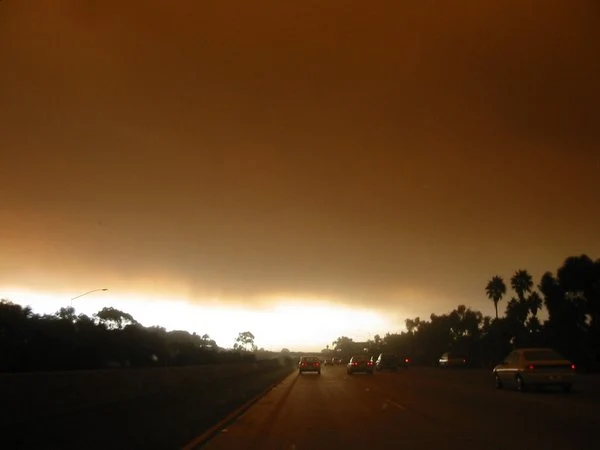 Orange smoke-filled sky over southbound Interstate 5 near Pacific Beach during the 2003 Cedar Fire, with headlights visible in freeway traffic